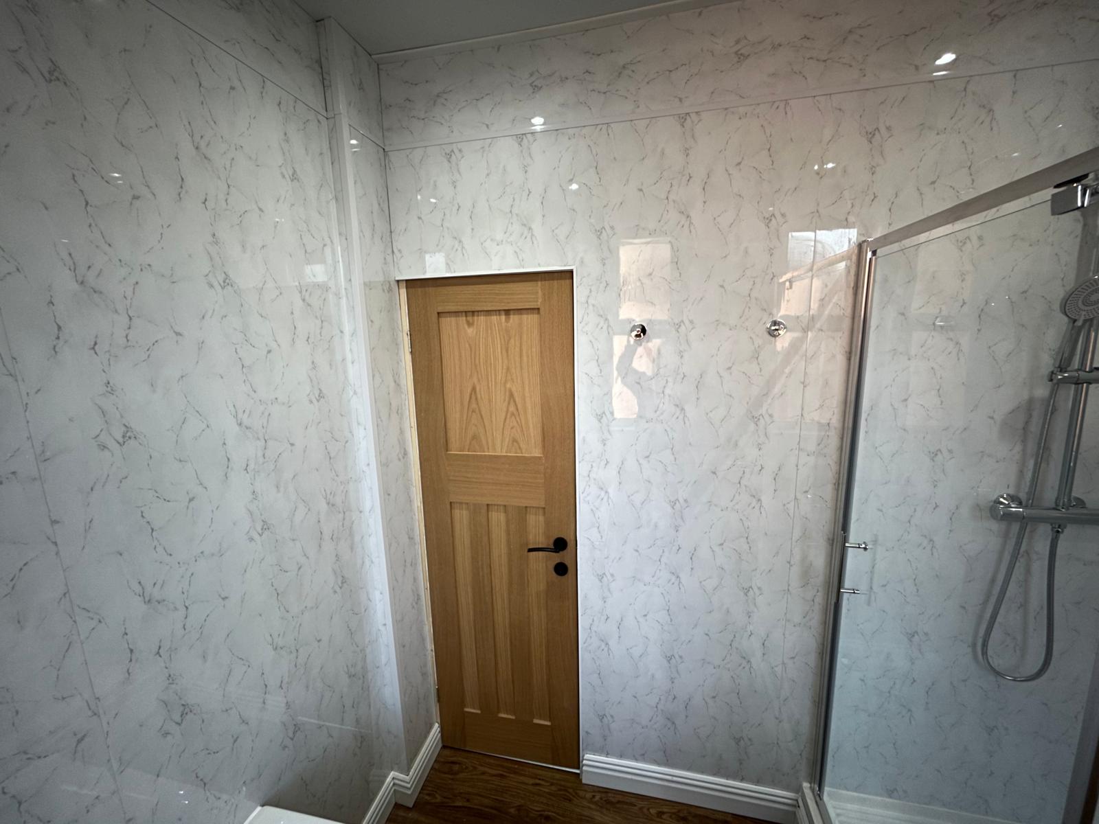 Bathroom with marble-effect wall panelling, oak door and glass shower enclosure