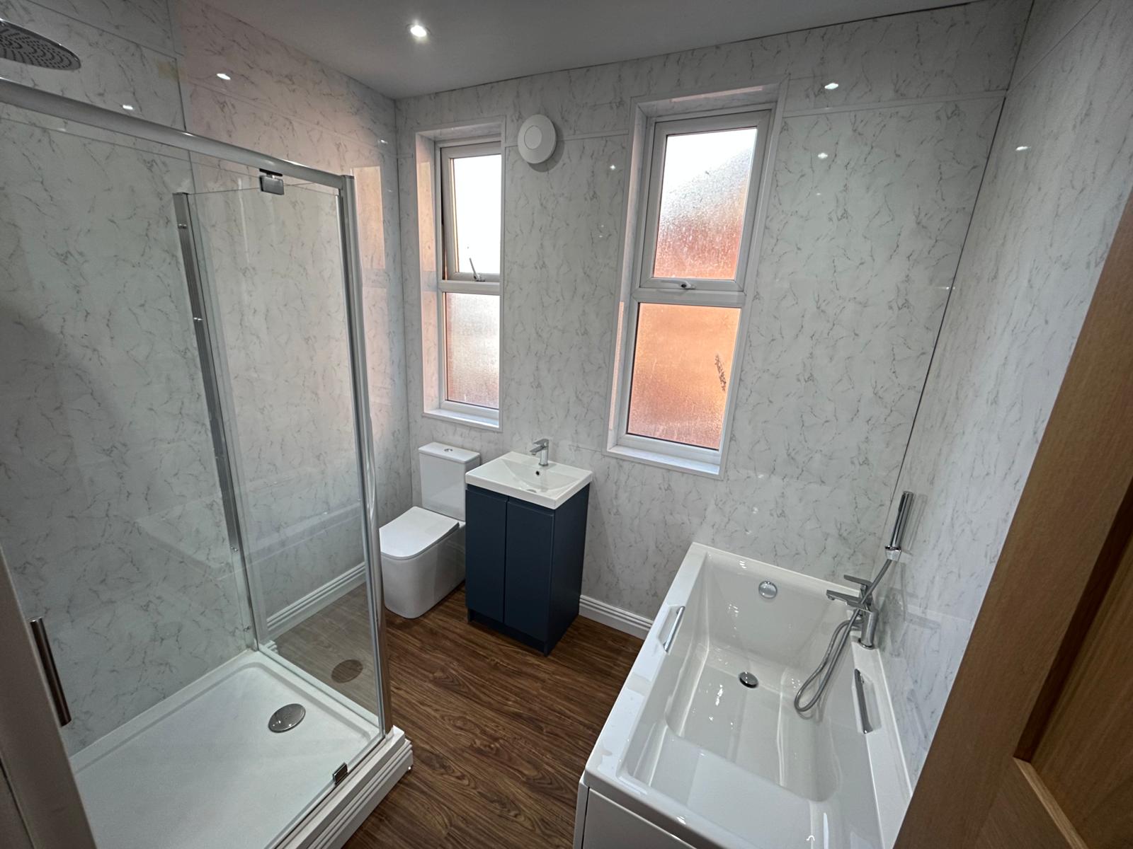 Refurbished bathroom with marble-effect wall panels, shower enclosure, bath and navy vanity unit
