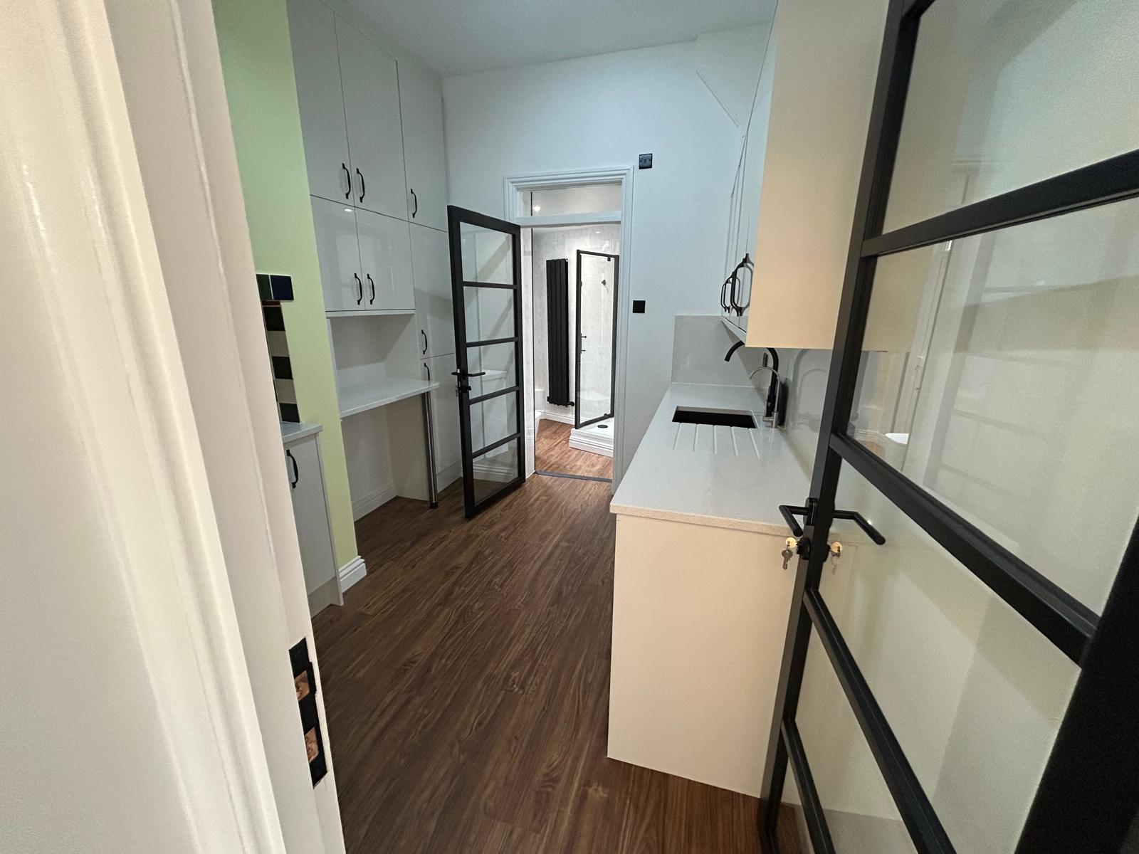 Galley kitchen with white gloss units, quartz worktops and a black Crittall-style glazed door