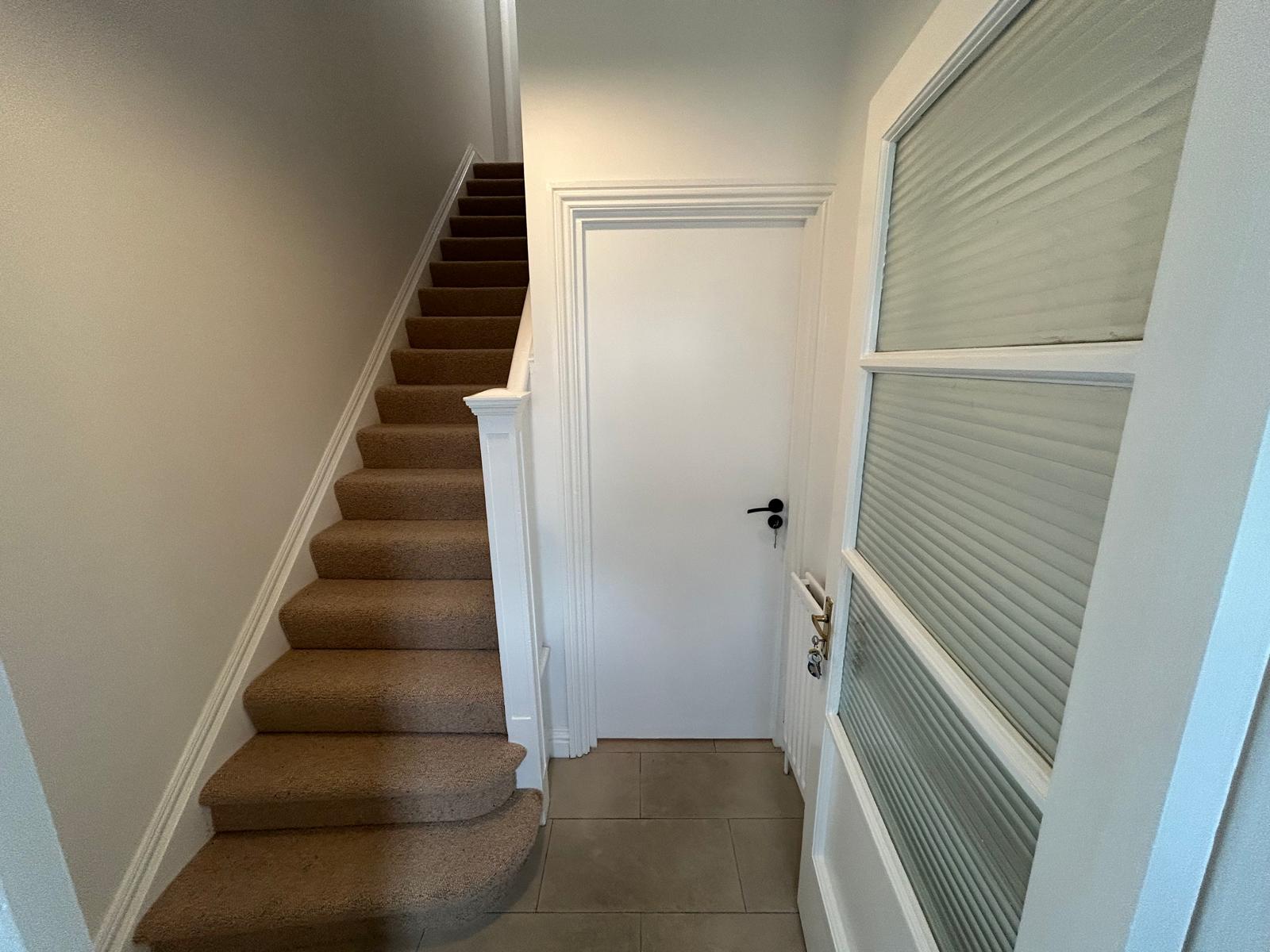 Hallway and staircase after a full house refurbishment, with new carpet, painted joinery and a glazed door
