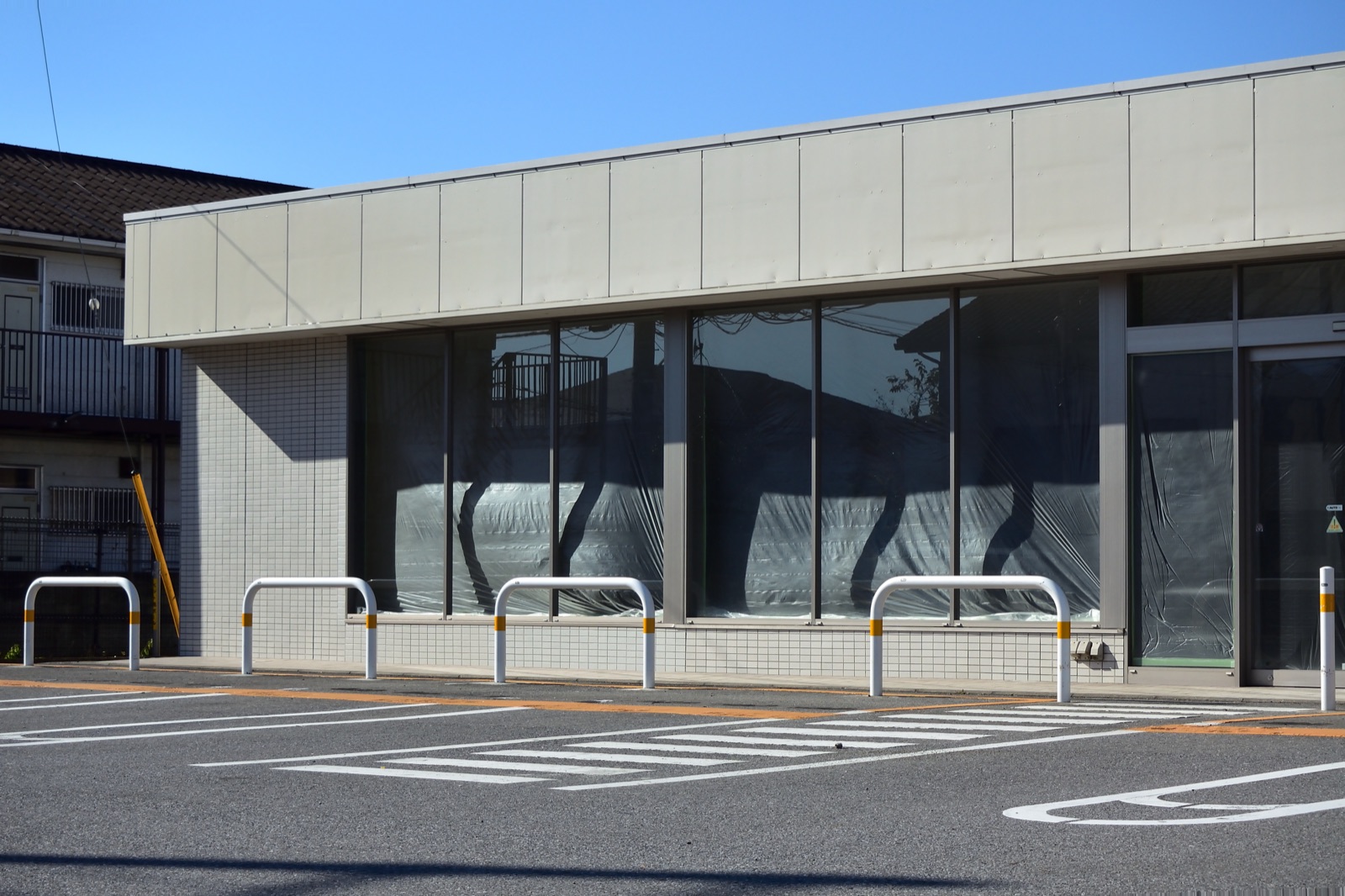 Single-storey retail unit with its shopfront glazing screened off with protective sheeting