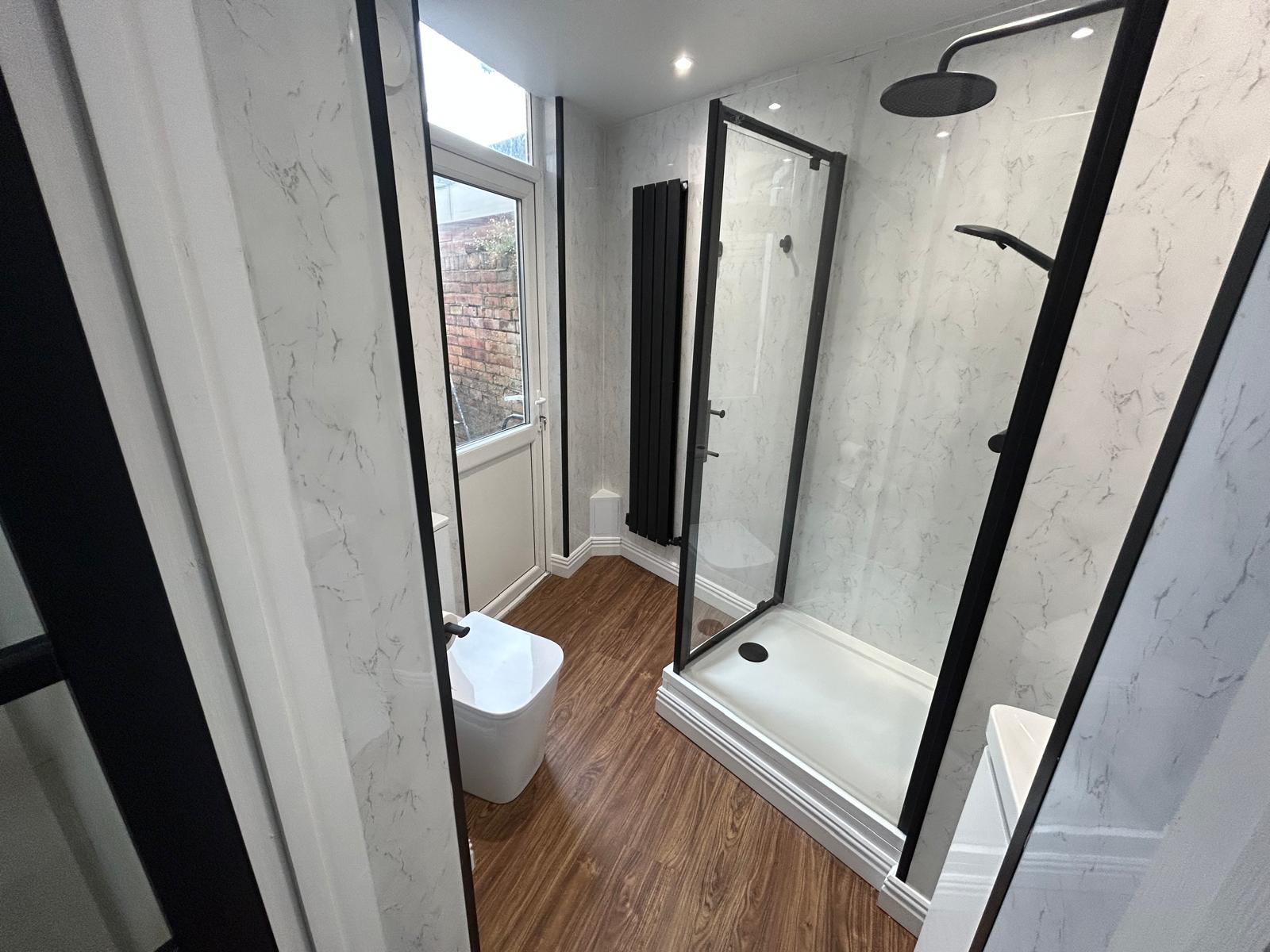 Shower room with marble-effect panels, matt black shower, radiator and door frames