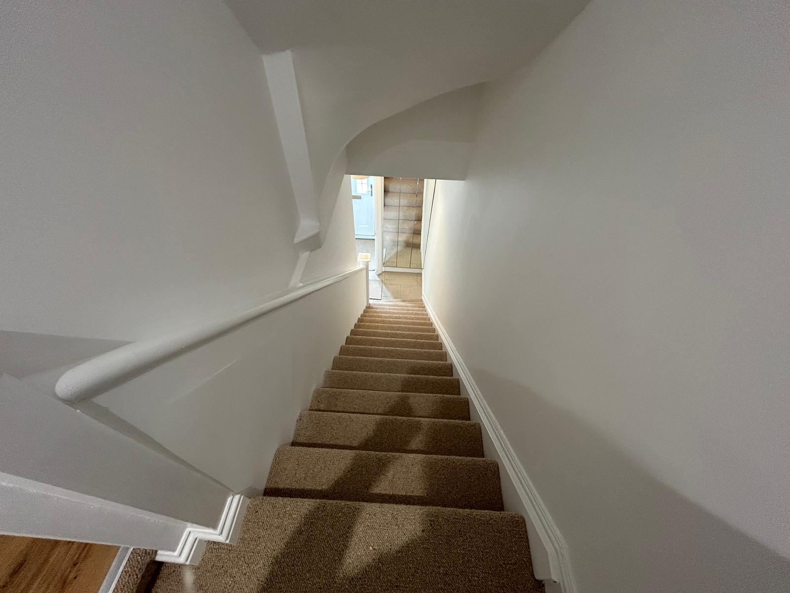 Staircase redecorated in white with new carpet, looking down to the front door