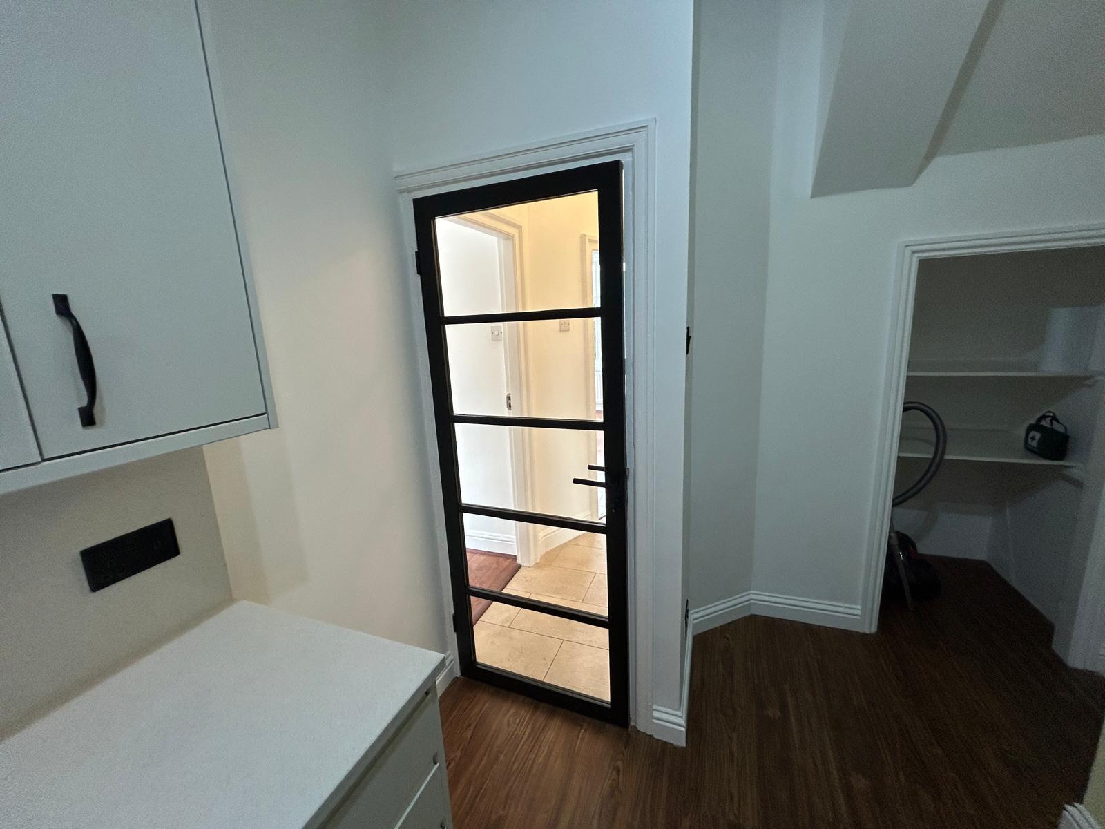 Utility room with glazed black-framed door and understairs pantry